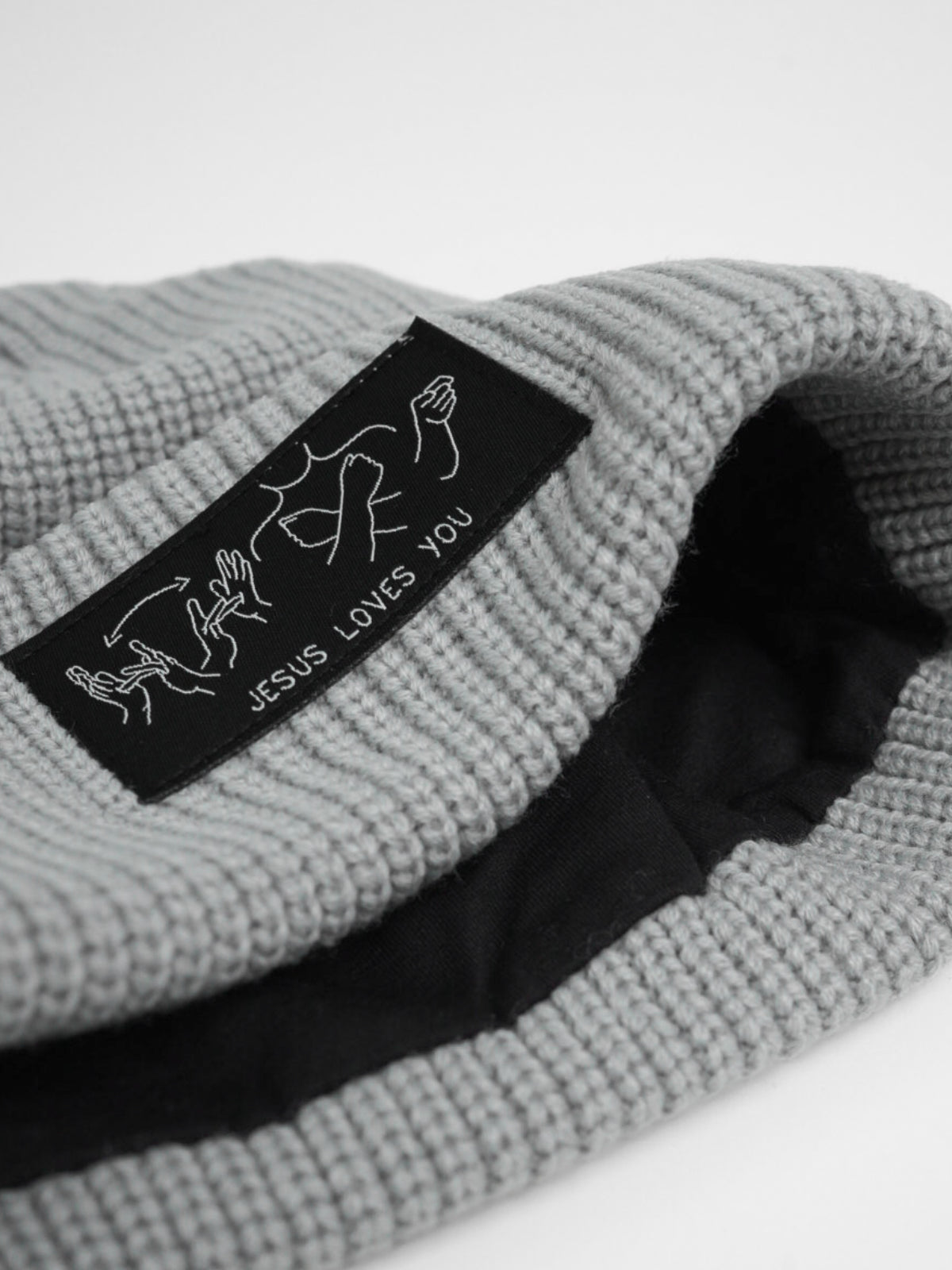Gray knit beanie with a black label reading 'Jesus Loves You' on a light gray background