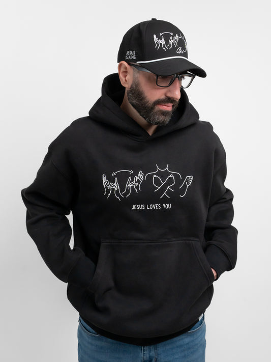 Man wearing a black hoodie and cap with white graphics and text on a light gray background