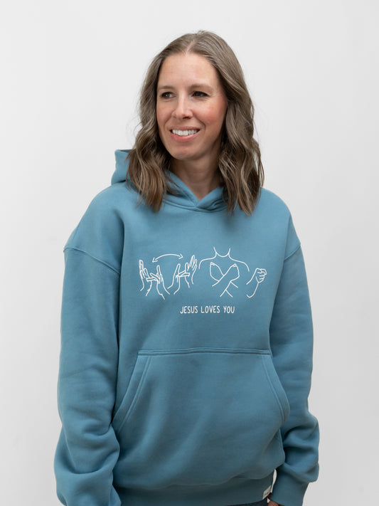 Person wearing a blue hoodie with 'Jesus Loves You' text and design on a white background