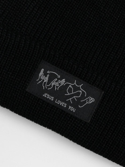 Black knit beanie with 'Jesus Loves You' tag on a black background