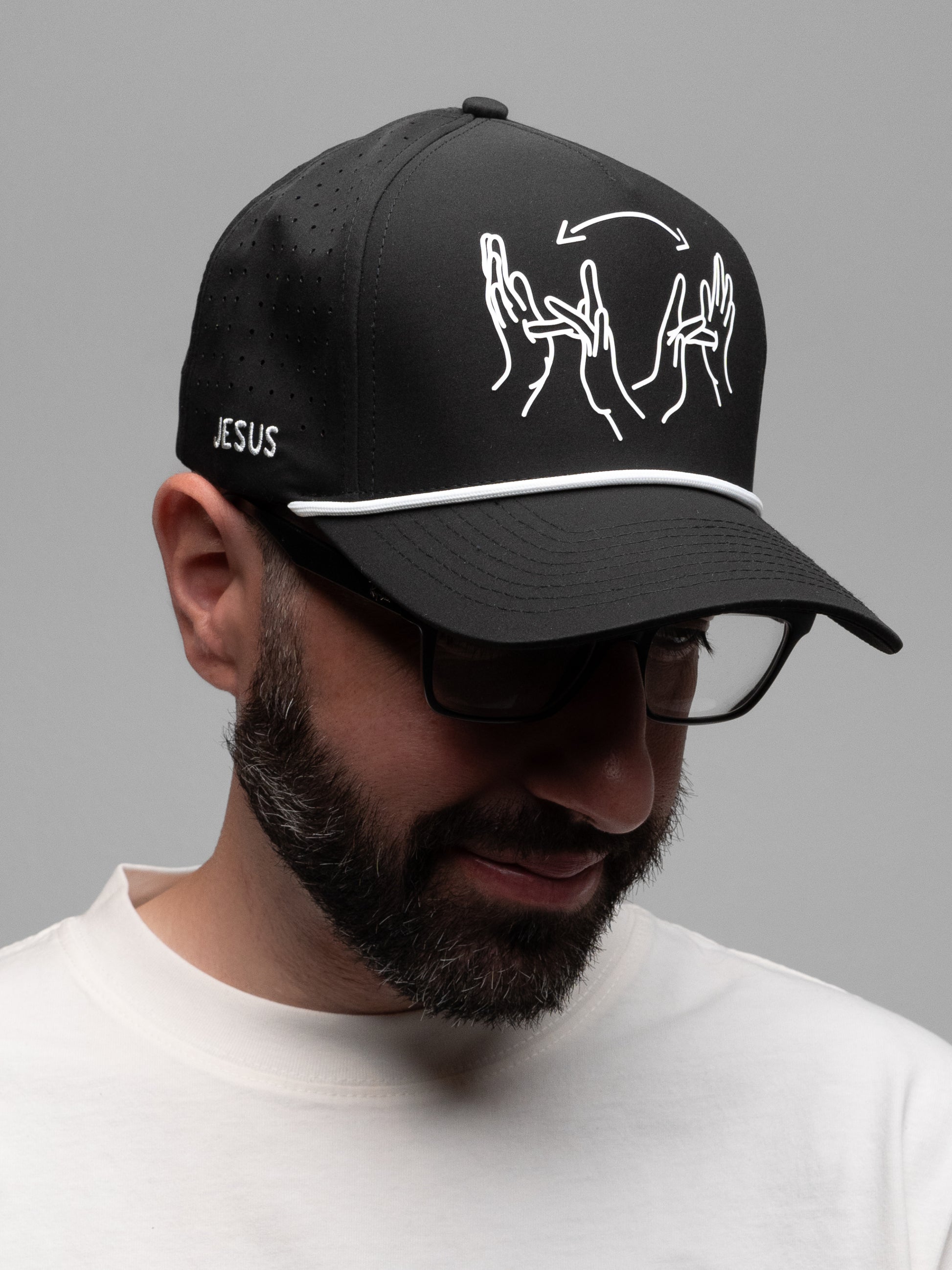 Man wearing a black cap with white designs and 'Jesus' text on a gray background