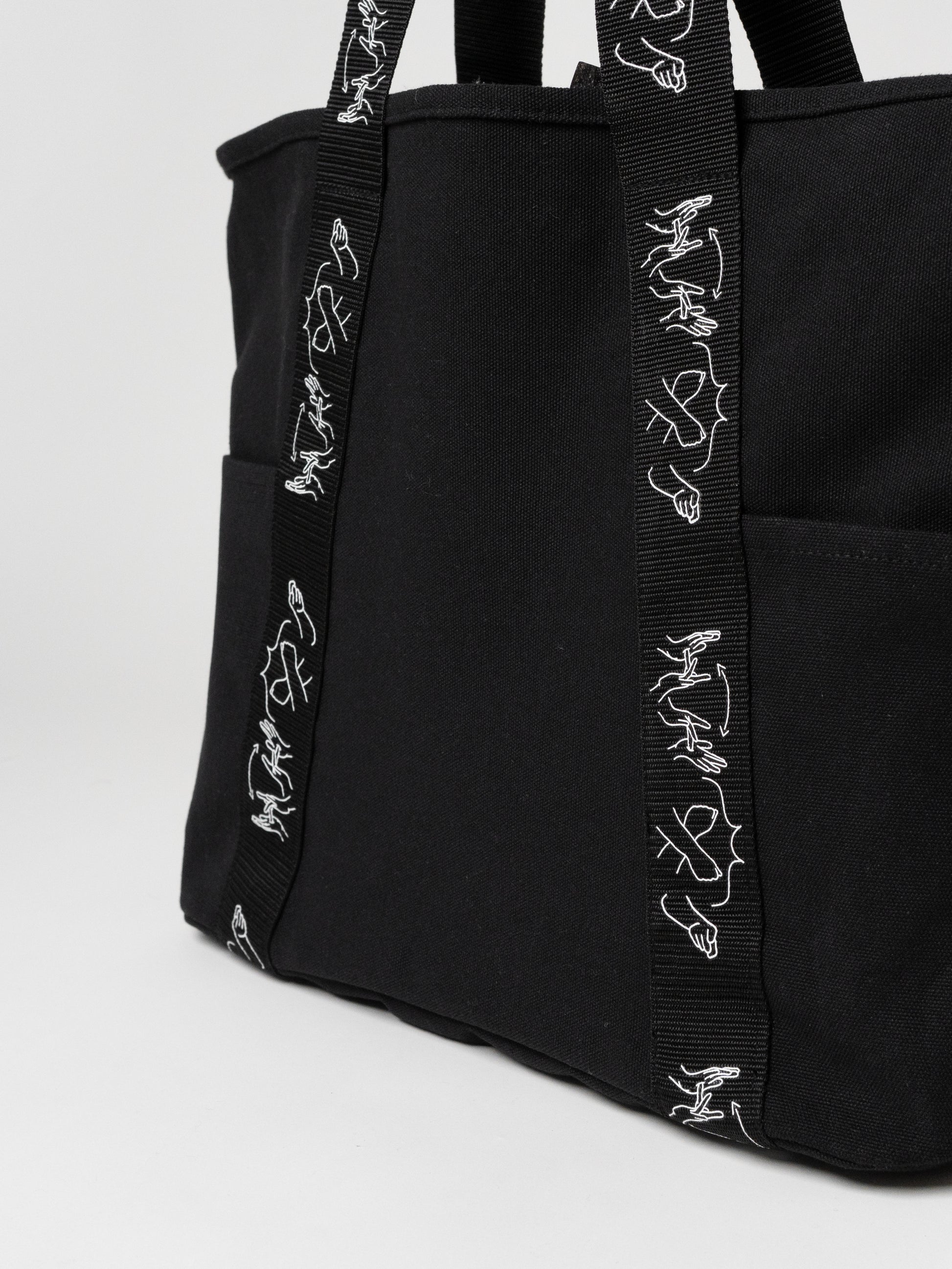 Black tote bag with decorative straps on a light gray background