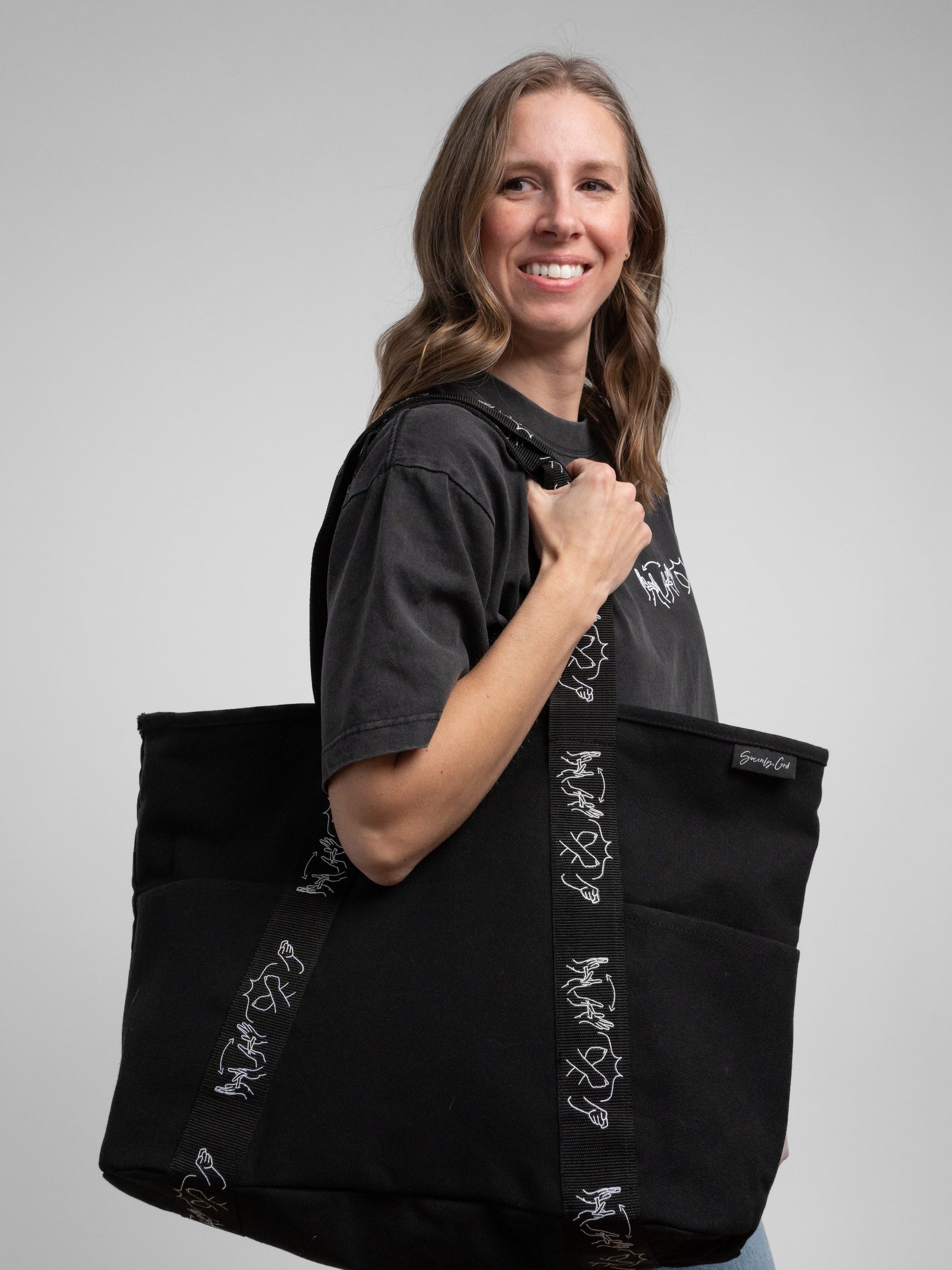 Woman holding a black tote bag with white designs against a gray background