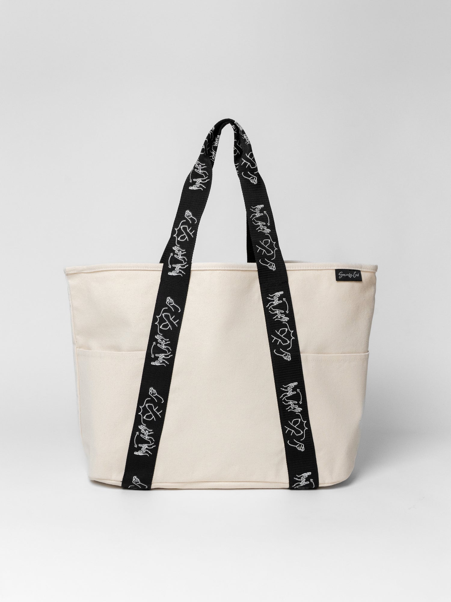 Beige tote bag with black straps featuring white text on a light gray background