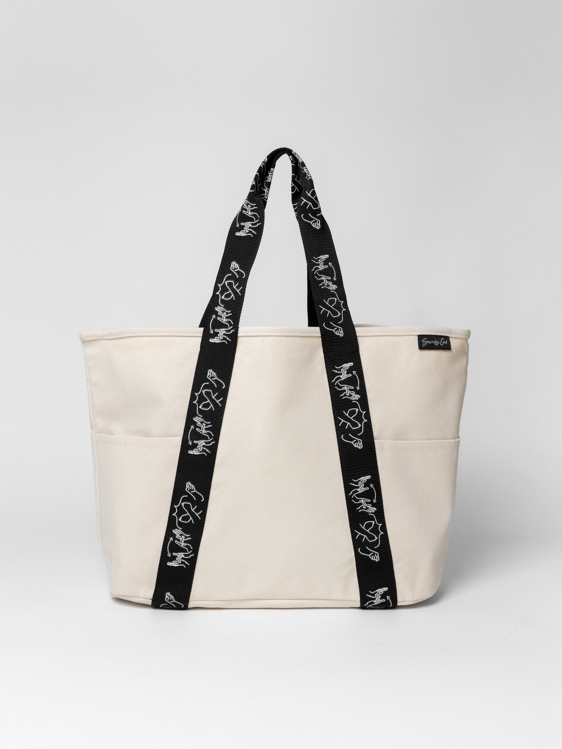 Beige tote bag with black straps featuring white text on a light gray background