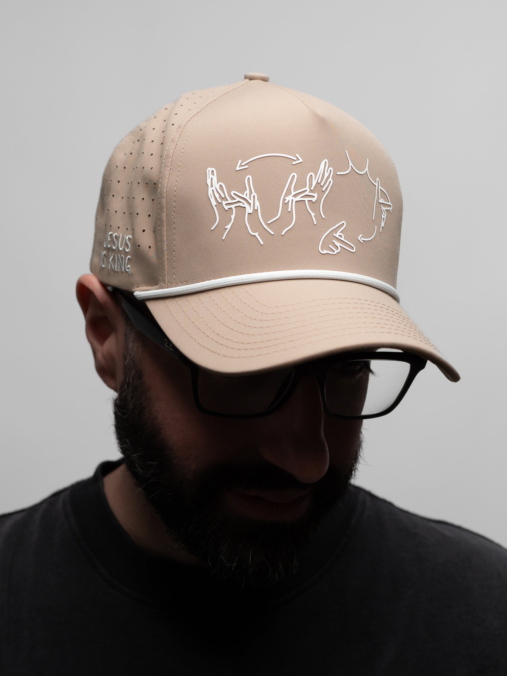 Beige cap with white embroidered design worn by a person on a gray background
