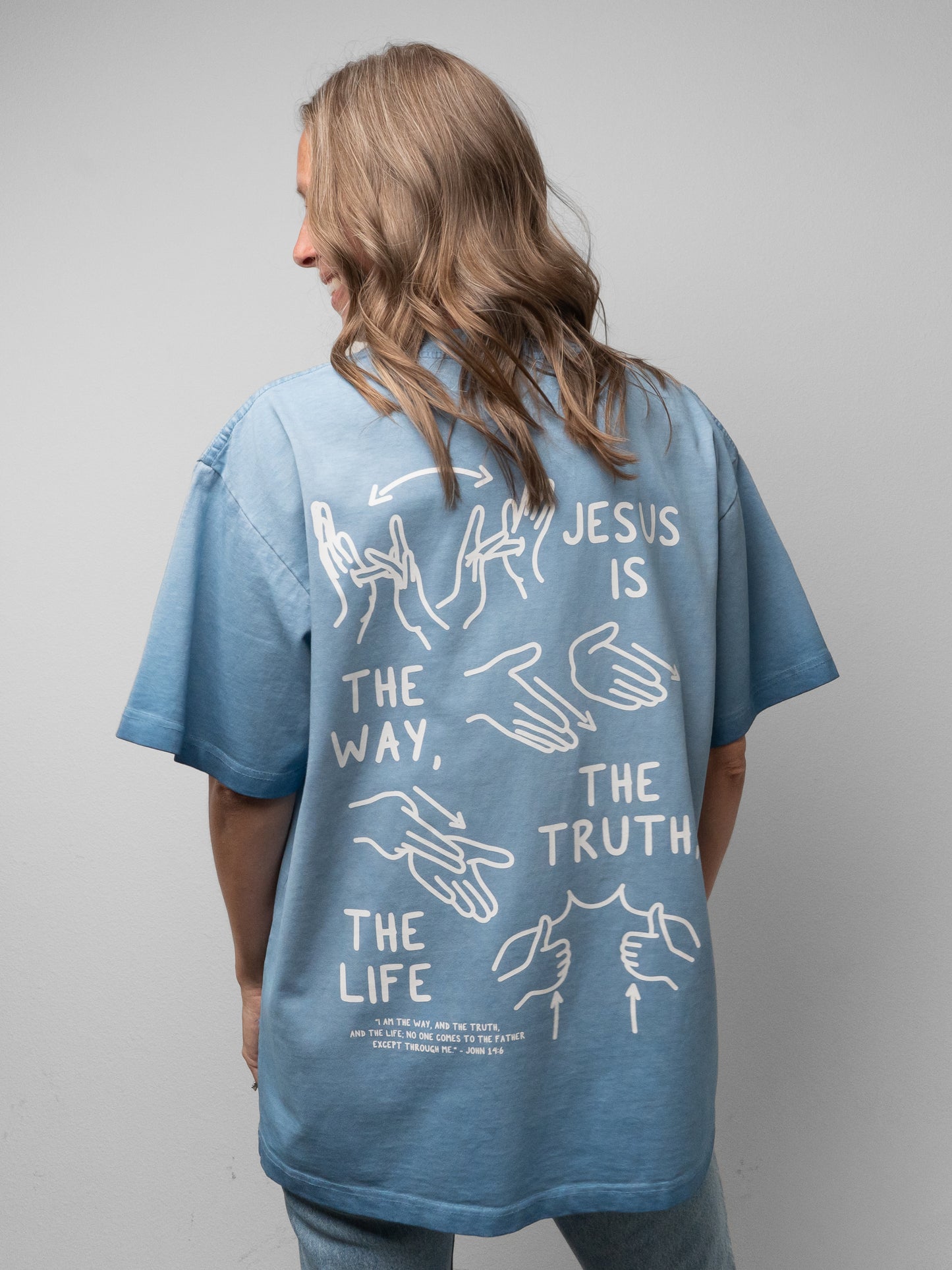Person wearing a blue t-shirt with a religious message on the back against a gray background